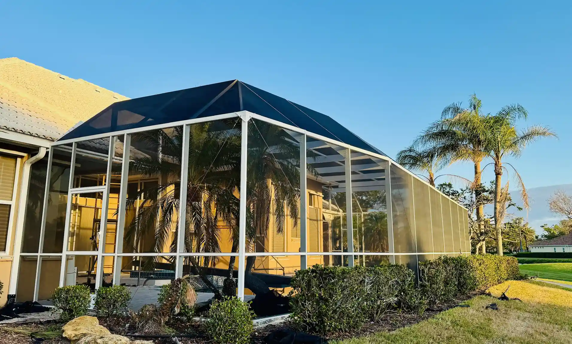 White aluminum Florida pool cage with dark screen panels and diagonal hurricane reinforcement cables